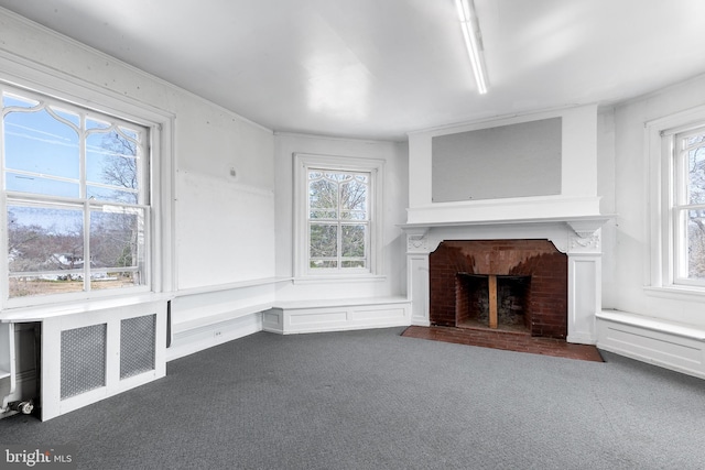 unfurnished living room with radiator heating unit, a fireplace, and dark carpet