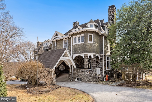 view of front of house with stone siding, driveway, and a chimney