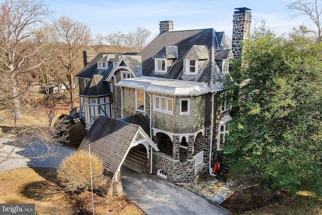 view of front of property with stone siding, driveway, and a chimney