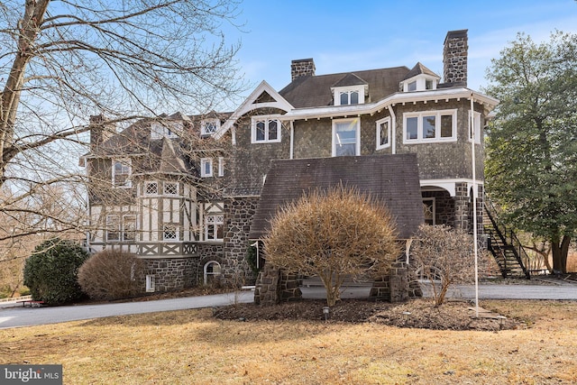 view of front of property featuring stairway, stone siding, and a chimney