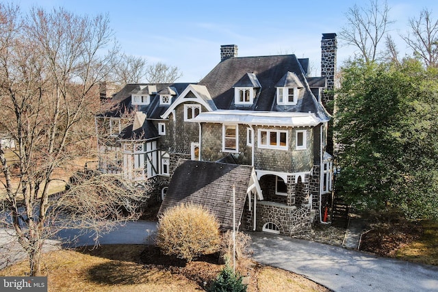 shingle-style home featuring aphalt driveway, stone siding, and a chimney