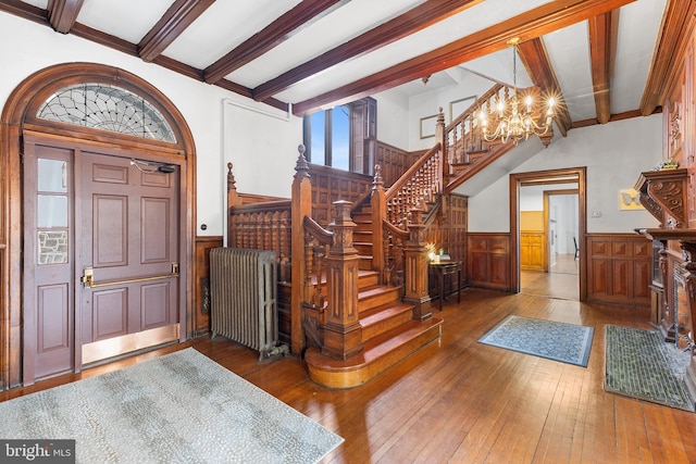 entryway featuring a wainscoted wall, a notable chandelier, hardwood / wood-style flooring, radiator heating unit, and stairway