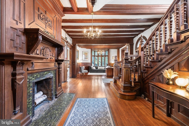 foyer with beam ceiling, hardwood / wood-style floors, stairway, an inviting chandelier, and a tile fireplace