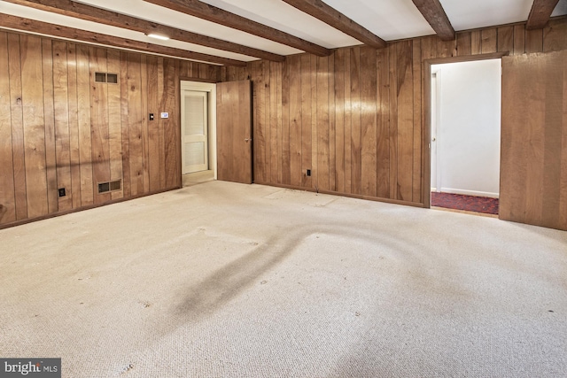 empty room with beamed ceiling, wooden walls, and visible vents