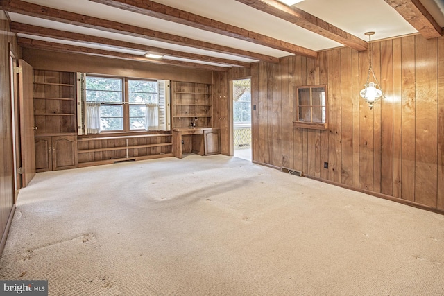 unfurnished living room with beam ceiling, visible vents, wood walls, and carpet floors