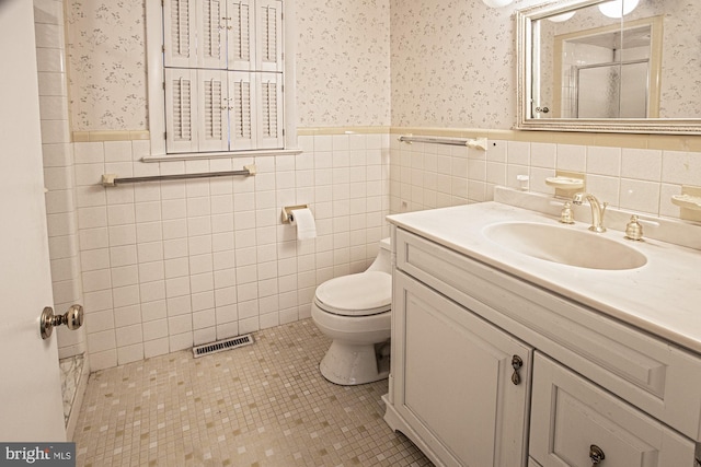 full bathroom featuring wallpapered walls, toilet, wainscoting, a stall shower, and vanity