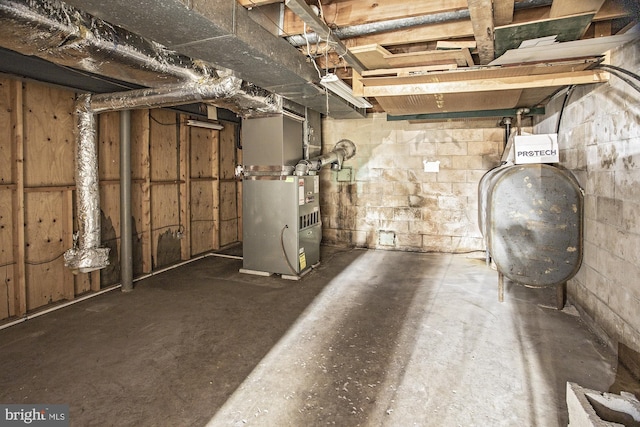 unfinished basement featuring concrete block wall, heating fuel, and heating unit