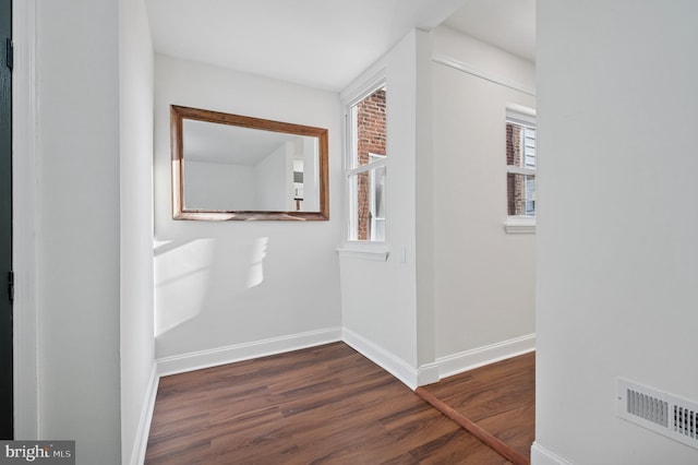 corridor featuring dark wood finished floors, baseboards, and visible vents