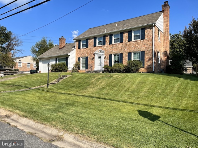 colonial-style house with a front yard, an attached garage, brick siding, and a chimney