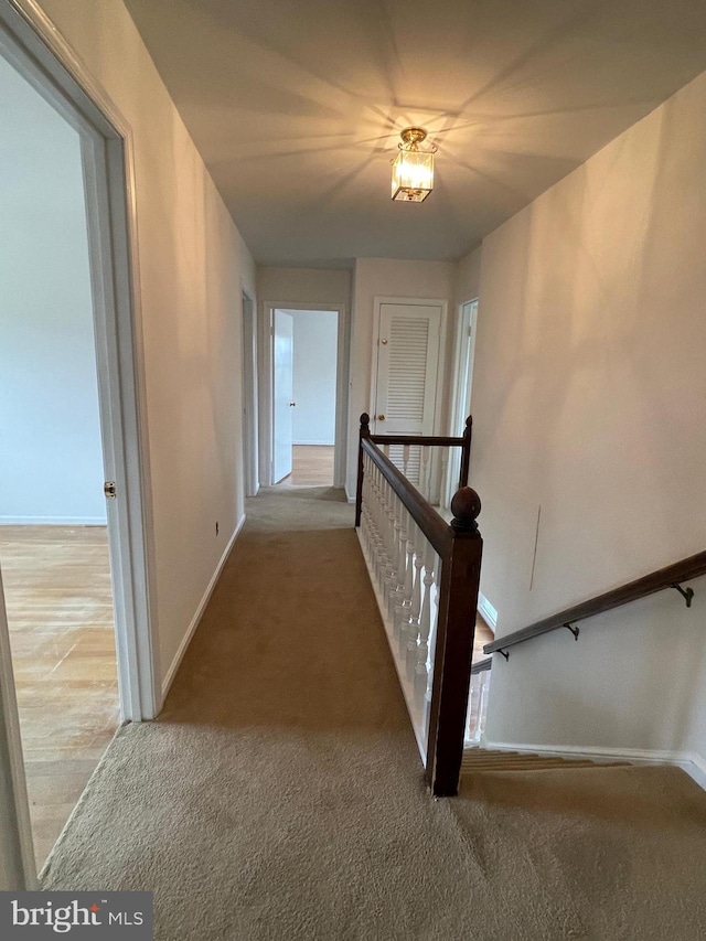 corridor with an upstairs landing, carpet flooring, and baseboards