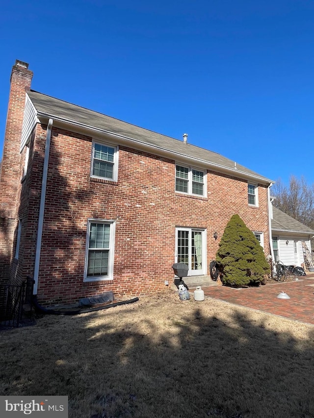 rear view of house with a yard, brick siding, and a chimney