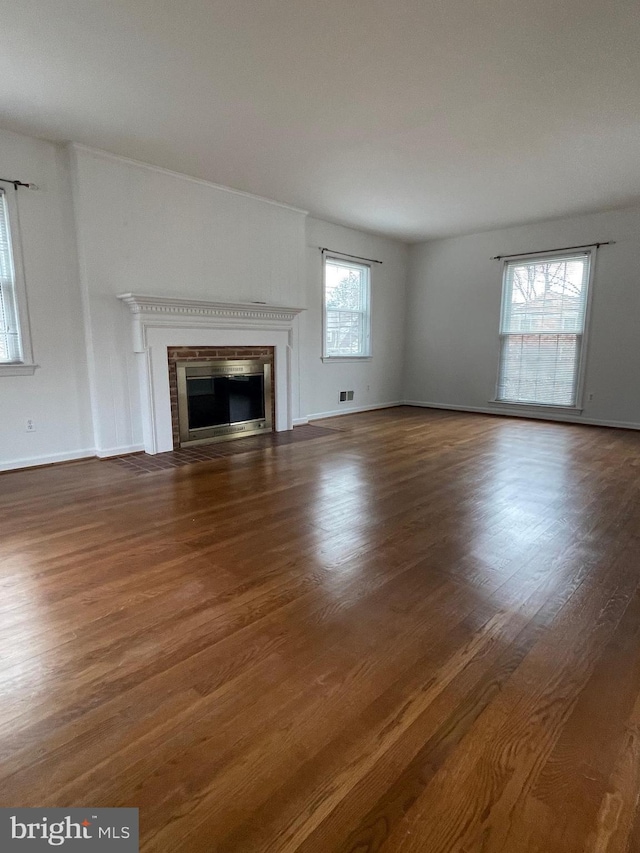 unfurnished living room with a glass covered fireplace, baseboards, visible vents, and wood finished floors