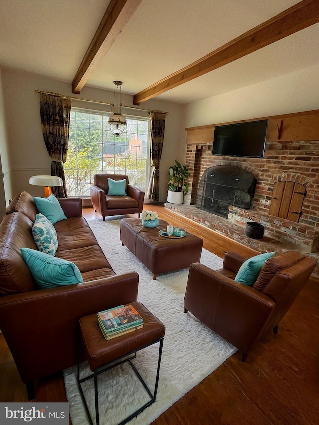 living area with beam ceiling, a brick fireplace, and wood finished floors