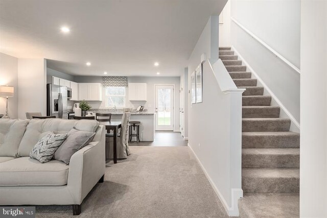 living area with recessed lighting, stairway, baseboards, and light colored carpet