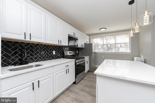 kitchen featuring light wood-style flooring, a sink, stainless steel appliances, white cabinets, and tasteful backsplash