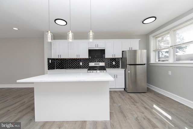 kitchen with light wood finished floors, a kitchen island, white cabinets, appliances with stainless steel finishes, and tasteful backsplash