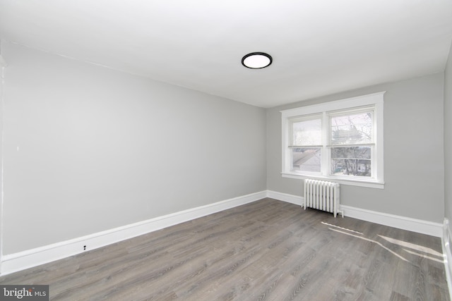 spare room with radiator heating unit, baseboards, and wood finished floors