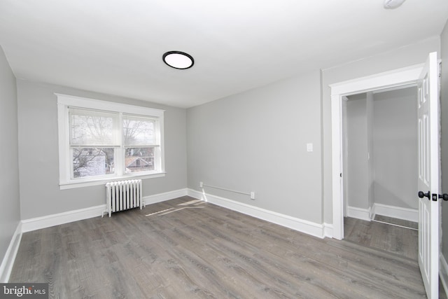 spare room with radiator heating unit, baseboards, and wood finished floors