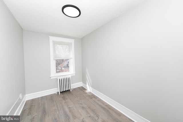 spare room with radiator, wood finished floors, and baseboards