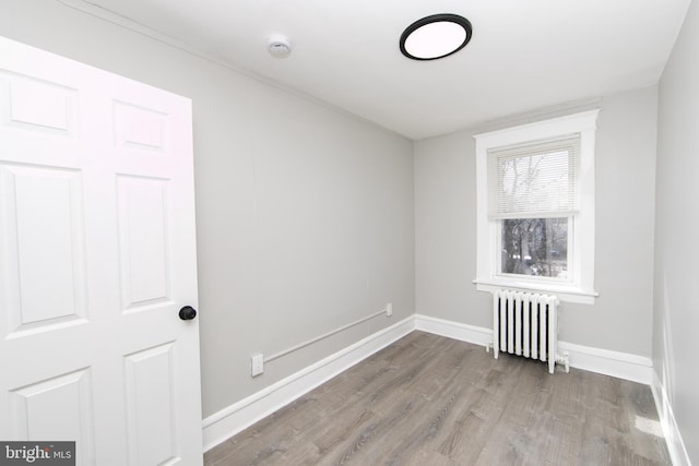 spare room featuring radiator heating unit, baseboards, and wood finished floors