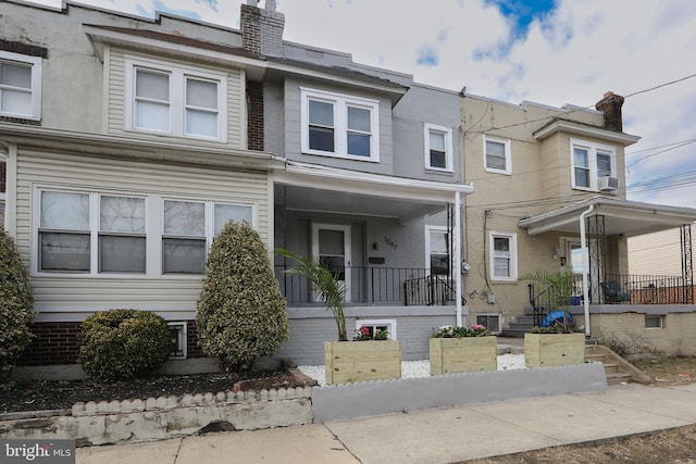 townhome / multi-family property with brick siding, covered porch, and a chimney