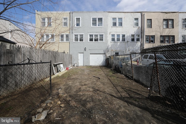 rear view of house featuring an attached garage, fence, and stucco siding