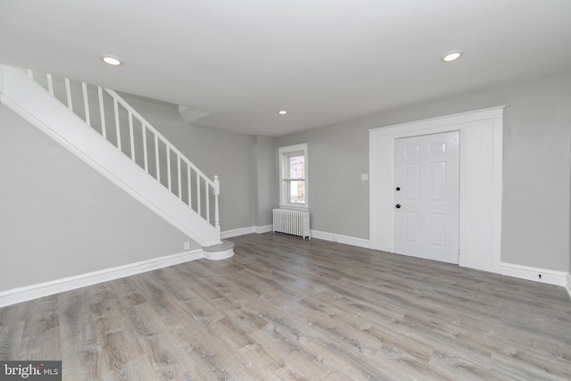 foyer entrance with stairs, radiator, wood finished floors, and baseboards