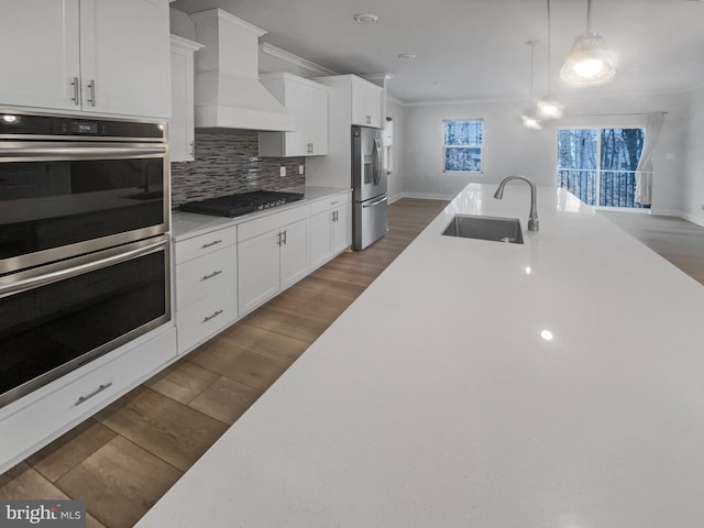 kitchen featuring wood finished floors, custom exhaust hood, stainless steel appliances, a sink, and light countertops