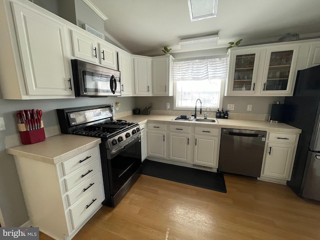 kitchen with light wood finished floors, vaulted ceiling, appliances with stainless steel finishes, white cabinetry, and a sink