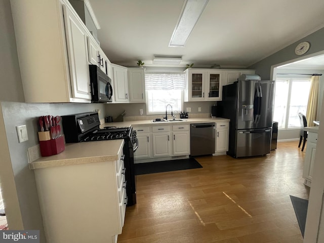 kitchen with wood finished floors, a sink, black appliances, light countertops, and white cabinetry