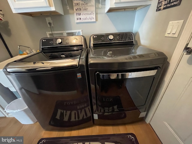 laundry area featuring wood finished floors, cabinet space, and washing machine and dryer