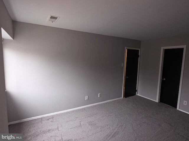 empty room with baseboards, visible vents, and dark carpet