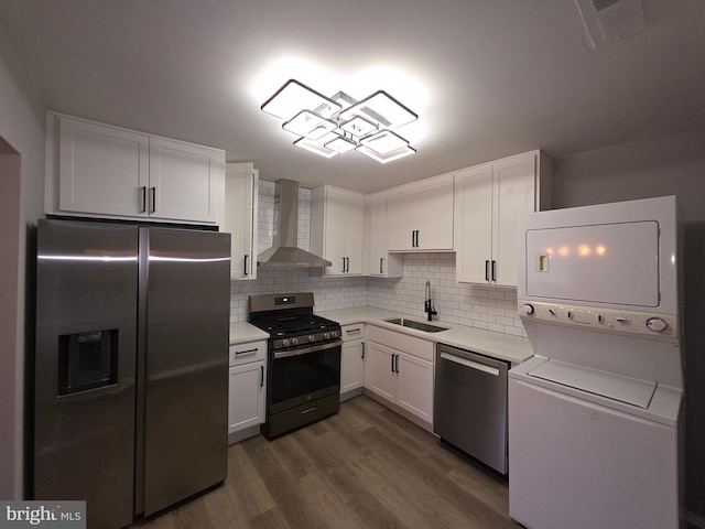 kitchen with a sink, stacked washing maching and dryer, stainless steel appliances, wall chimney exhaust hood, and light countertops