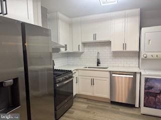 kitchen with light countertops, stacked washer and dryer, stainless steel appliances, white cabinetry, and a sink