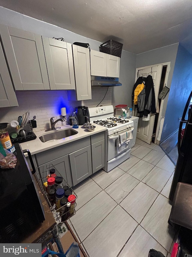 kitchen featuring white range with gas cooktop, a sink, light countertops, under cabinet range hood, and tasteful backsplash