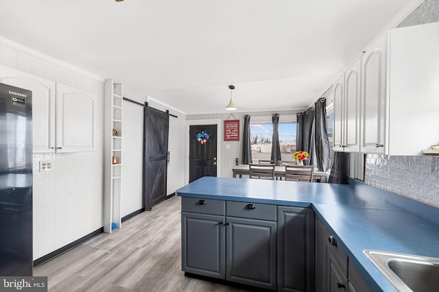 kitchen with a peninsula, light wood-style flooring, decorative backsplash, white cabinetry, and a barn door