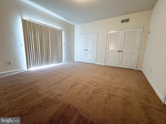 unfurnished bedroom with visible vents, baseboards, multiple closets, and carpet floors