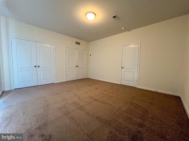 unfurnished bedroom featuring carpet, visible vents, two closets, and baseboards