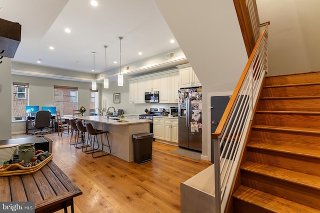 kitchen featuring a kitchen island with sink, light wood-type flooring, light countertops, appliances with stainless steel finishes, and a sink