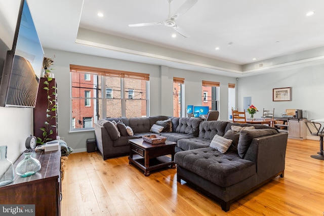 living room featuring recessed lighting, light wood-type flooring, a raised ceiling, and a ceiling fan