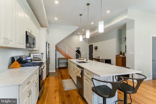 kitchen with light wood finished floors, a breakfast bar area, stainless steel appliances, and a sink