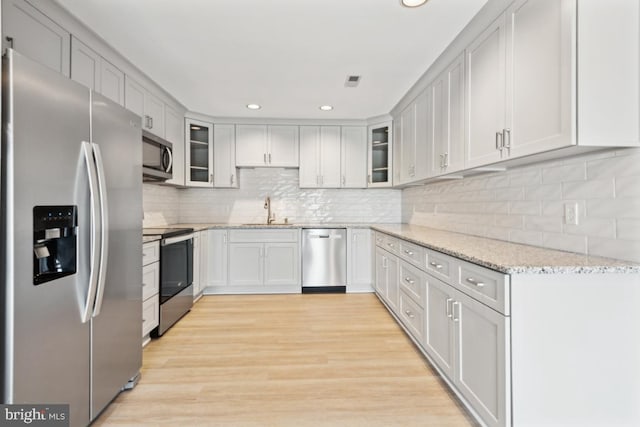 kitchen with glass insert cabinets, light stone counters, appliances with stainless steel finishes, light wood-style floors, and a sink