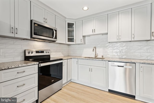 kitchen with a sink, stainless steel appliances, light wood-style floors, and tasteful backsplash