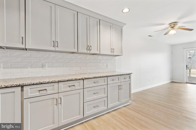 kitchen with tasteful backsplash, light wood finished floors, baseboards, light stone counters, and a ceiling fan