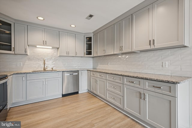 kitchen with gray cabinetry, light wood-type flooring, decorative backsplash, stainless steel dishwasher, and a sink