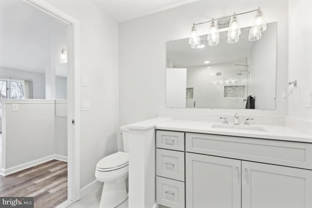 bathroom featuring baseboards, toilet, wood finished floors, vanity, and a shower