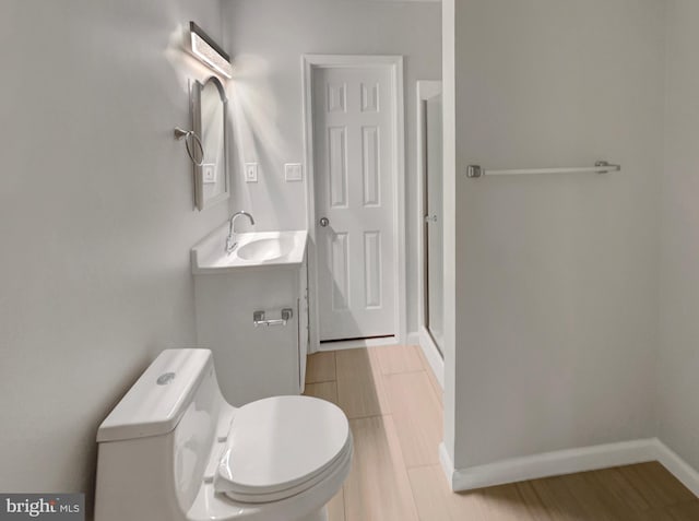 bathroom with baseboards, toilet, a stall shower, wood finished floors, and vanity