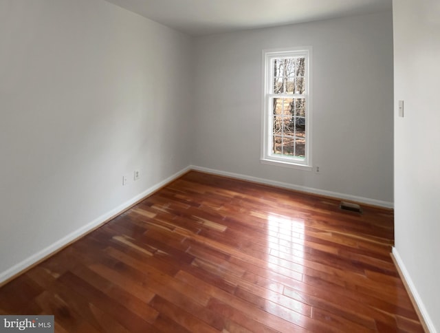 empty room with baseboards, wood-type flooring, and visible vents