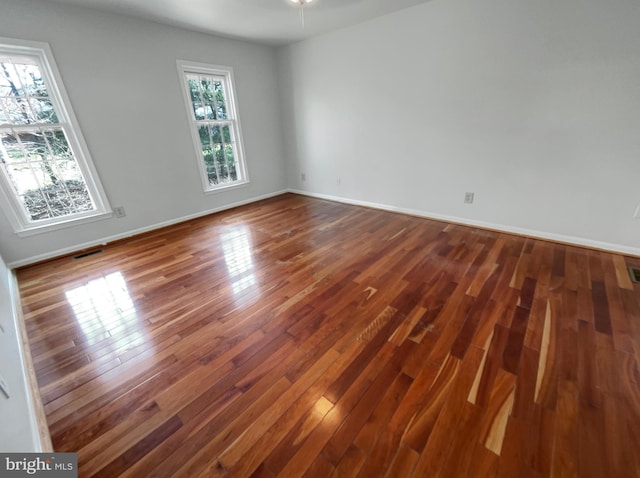 empty room featuring dark wood-style floors, visible vents, and baseboards