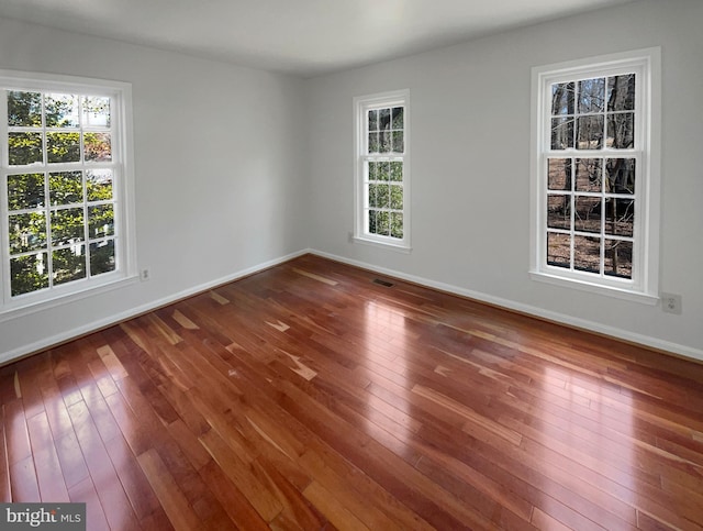 empty room featuring plenty of natural light, visible vents, baseboards, and wood-type flooring